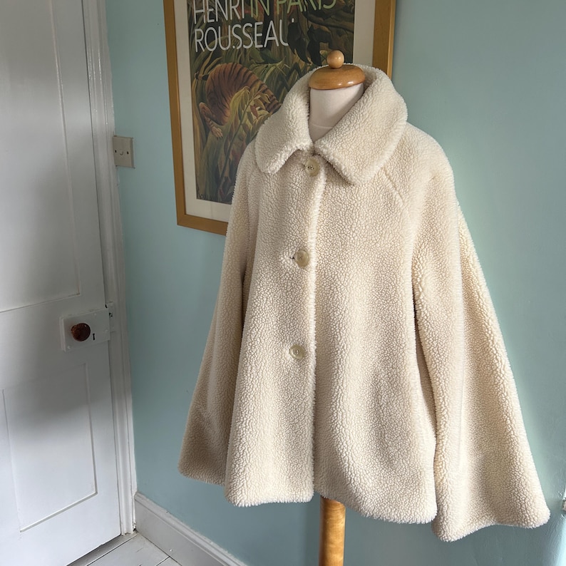 May include: A cream-colored, fluffy, faux fur jacket with a button closure and a slightly flared silhouette.