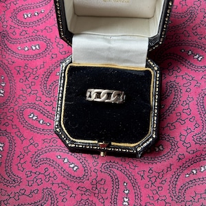 May include: A silver chain ring in a black velvet ring box. The ring is made of interlocking chain links.