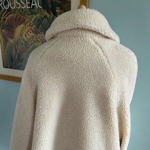 May include: A white faux fur jacket with a high collar and long sleeves. The jacket is made of a soft, fluffy material and has a relaxed fit.