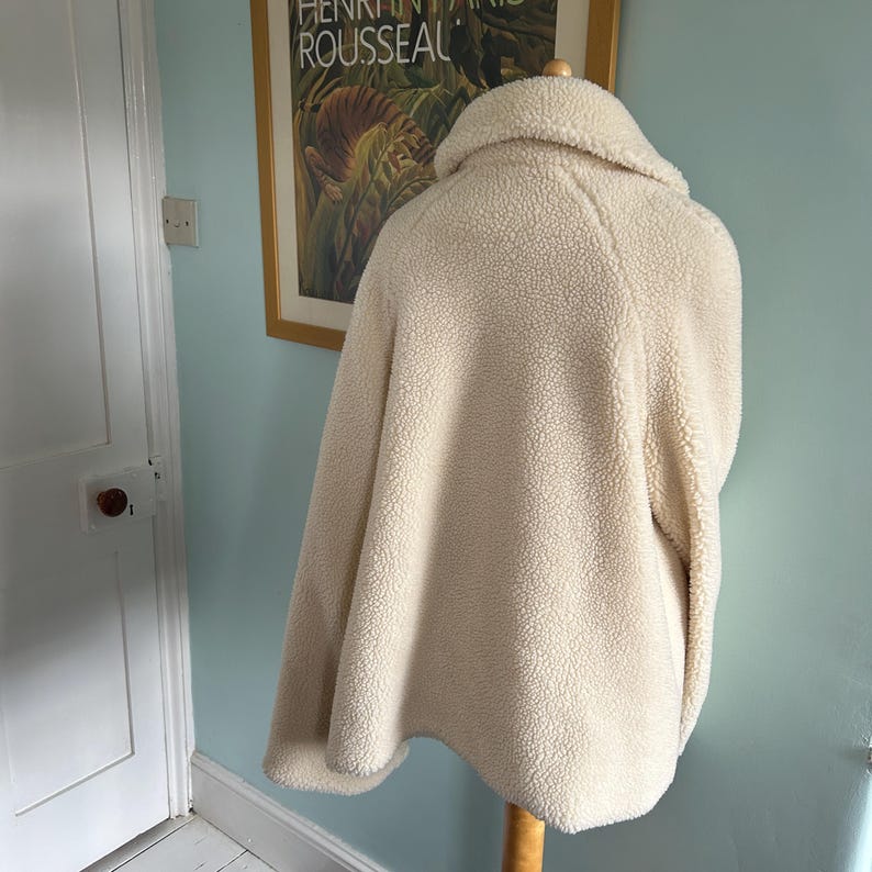 May include: A cream-colored faux fur jacket with a high collar and long sleeves.