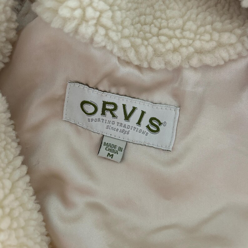 May include: A white fleece jacket with a brown Orvis label that reads "Sporting Traditions Since 1856". The label also has a smaller label that says "Made in China M".
