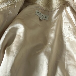 May include: A cream-colored jacket with a soft, fuzzy lining. The jacket has a label that reads "ORVIS" and "Made in China".