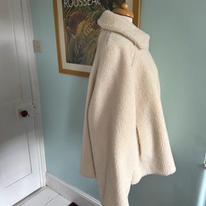 May include: A cream-colored, fluffy, faux fur jacket with a zipper closure. The jacket has a collar and long sleeves.