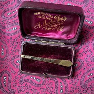 Vintage gold tone tie clip in the shape of a tie.