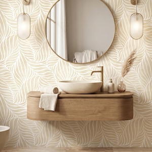 May include: A bathroom vanity area featuring a floating light wood cabinet with a white oval vessel sink and a gold faucet. Above, a round mirror is flanked by two vertical frosted glass wall sconces against a beige and white leaf-patterned wallpaper.