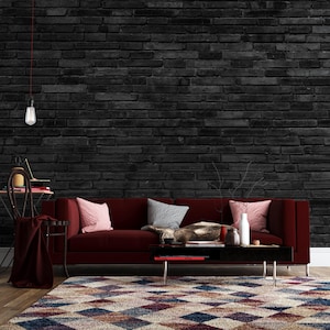 Puede incluir: Un sofá de terciopelo rojo con almohadas y una manta se encuentra frente a una pared de ladrillo negro. Una mesa de centro con algunos artículos decorativos se encuentra frente al sofá. Una alfombra estampada cubre el suelo.