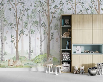 May include: A light-colored wooden storage unit with open shelving and closed cabinets stands against a wall covered in forest-themed wallpaper featuring watercolor trees, green bushes, and small animals. Two small white stools sit in front.