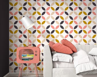 Puede incluir: Una pared blanca con un patrón geométrico repetitivo de círculos superpuestos en amarillo mostaza, rosa empolvado y gris carbón. Una mesa auxiliar rosa coral con forma de televisor sostiene una lámpara blanca y libros junto a un sofá.