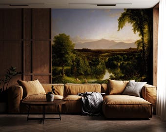 May include: A large-scale landscape mural featuring a river winding through a lush green valley toward distant mountains, displayed on a wall behind a tan sectional sofa with a round wooden coffee table and a gray throw blanket.