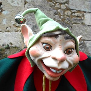 Könnte beinhalten: Eine grüne und rote Elfenpuppe mit einem großen, zahnigen Grinsen und einem grünen Hut mit einer Glocke. Die Puppe trägt ein grünes und rotes Kostüm.