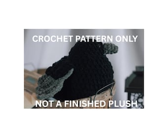 May include: A black and dark gray crocheted bird figure with a rounded body and textured wings. The text CROCHET PATTERN ONLY and NOT A FINISHED PLUSH is overlaid in white capital letters across the top and bottom of the image.