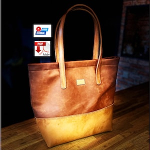 Pode incluir: Uma bolsa tote de couro marrom em dois tons com uma seção superior mais escura e um painel inferior mais claro, duas alças verticais de ombro e um pequeno remendo retangular de couro na frente. A imagem inclui ícones de tutorial em vídeo e PDF.