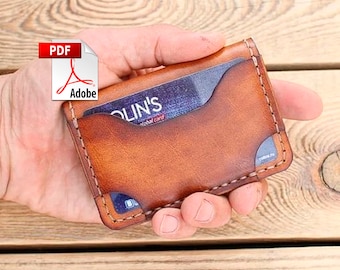 May include: A handcrafted, brown leather card wallet with visible stitching. The wallet has two card slots and a pocket holding a credit card. The Adobe PDF icon is in the upper left corner.