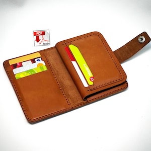 May include: A tan leather wallet featuring a snap-button closure strap, multiple interior card slots, and visible stitching along the edges. The wallet is shown open with several colorful credit cards inserted into the slots and a PDF icon visible.