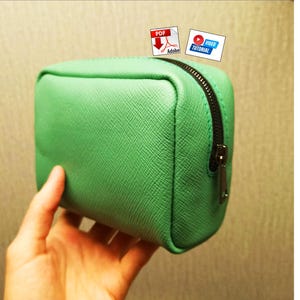 May include: A mint green rectangular zippered pouch with a textured crosshatch surface. The pouch features a dark metal zipper closure along the top and side. Two small icons are visible at the top, one labeled PDF and one labeled VIDEO TUTORIAL.