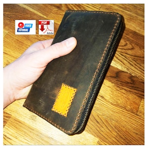 May include: A dark brown leather wallet featuring a rectangular yellow leather patch stitched onto the front surface. The wallet is secured with a black zipper along the edge and displays visible stitching details throughout the exterior construction.