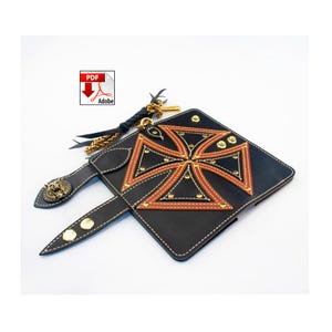 May include: Black leather wallet with a brown and gold cross design. The wallet features gold rivets, white stitching, and a decorative lion head clasp. A PDF Adobe icon is visible in the upper left corner. A black leather strap with gold chain and tassel is attached.