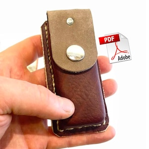 May include: A brown leather sheath with a suede flap secured by a silver snap. The sheath is held in a hand and has a contrasting light brown suede flap. The PDF Adobe logo is in the upper right corner.