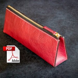 Op de afbeelding: Een rood leren etui met een zwarte rits en witte stiksels.