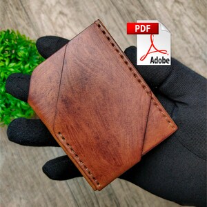 May include: A brown leather wallet with a folded design and stitched edges. The wallet is held in a hand wearing a black glove.