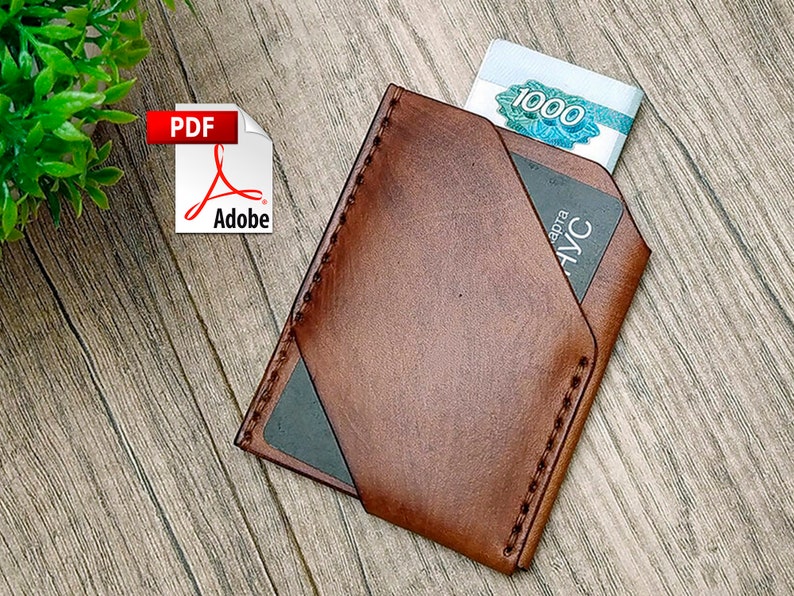 May include: A brown leather wallet with a stitched edge and a flap that folds over to secure the contents. The wallet has a black card slot and a billfold. The wallet is on a wooden surface.