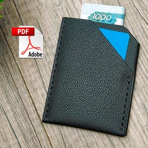 May include: Black leather wallet with a blue accent and a slot for cash. The wallet is on a wood surface. The text "1000" is visible on the cash.