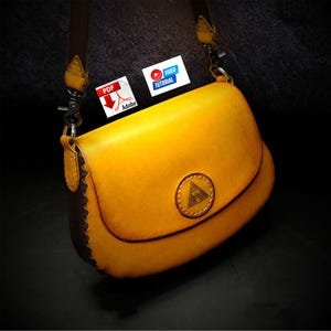 May include: A handcrafted yellow leather crossbody bag with a flap closure. The bag features a brown trim and strap, with a decorative emblem on the front. Includes PDF and Video Tutorial icons.