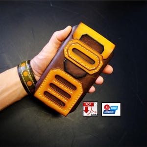 May include: Handmade brown leather phone case with tan accents and decorative stitching. The case features a unique design with geometric cutouts and a contrasting tan top. A matching leather bracelet is visible in the background.