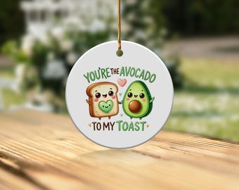 May include: White ceramic ornament with a cartoon avocado and toast holding hands. The text reads "You're the avocado to my toast".