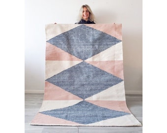 May include: A large, geometric rug with a white background and a pattern of pink and blue diamonds. The rug is made of a soft, woven material.