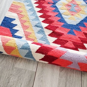 May include: A rolled up colourful rug with a geometric pattern in shades of pink, red, blue, yellow, and white.