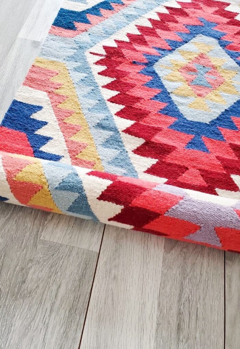 May include: A rolled up colourful rug with a geometric pattern in shades of pink, red, blue, yellow, and white.
