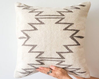 Puede incluir: Una almohada blanca con un patrón geométrico gris. La almohada está hecha de una tela suave y tejida.