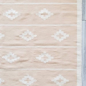 May include: A light pink rug with a white diamond pattern. The rug has a fringed border.