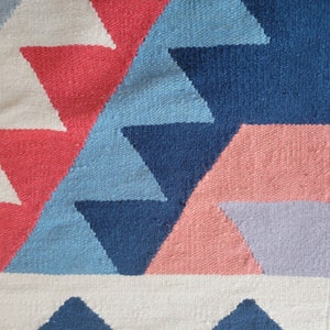 May include: A colourful geometric rug with a pattern of triangles in shades of blue, pink, red, and white.