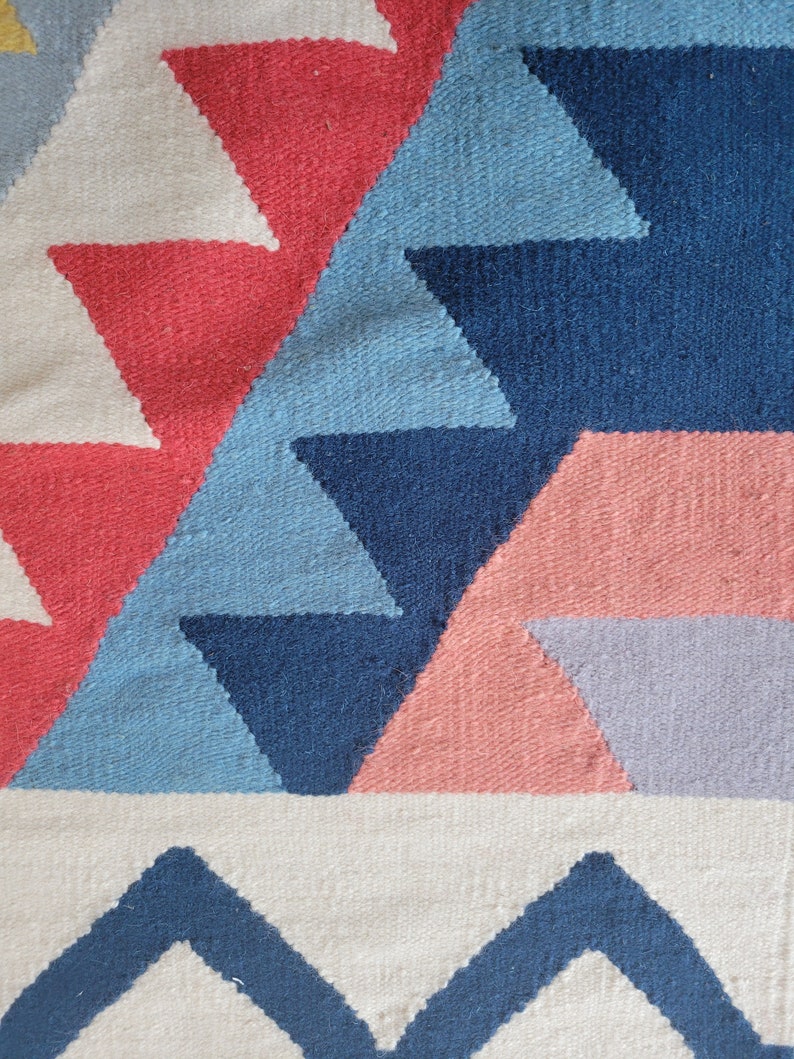 May include: A colourful geometric rug with a pattern of triangles in shades of blue, pink, red, and white.