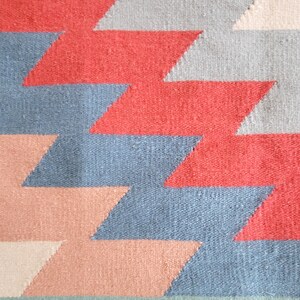 May include: A woven rug with a geometric pattern in shades of red, blue, green, and pink.