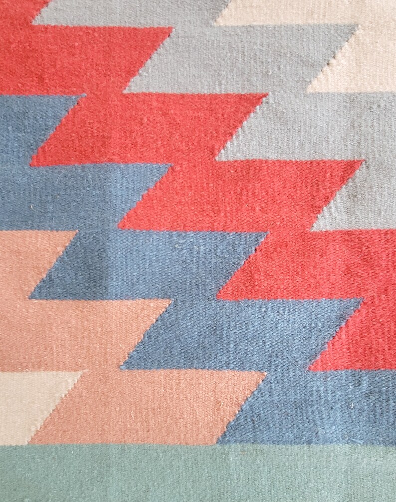 May include: A woven rug with a geometric pattern in shades of red, blue, green, and pink.