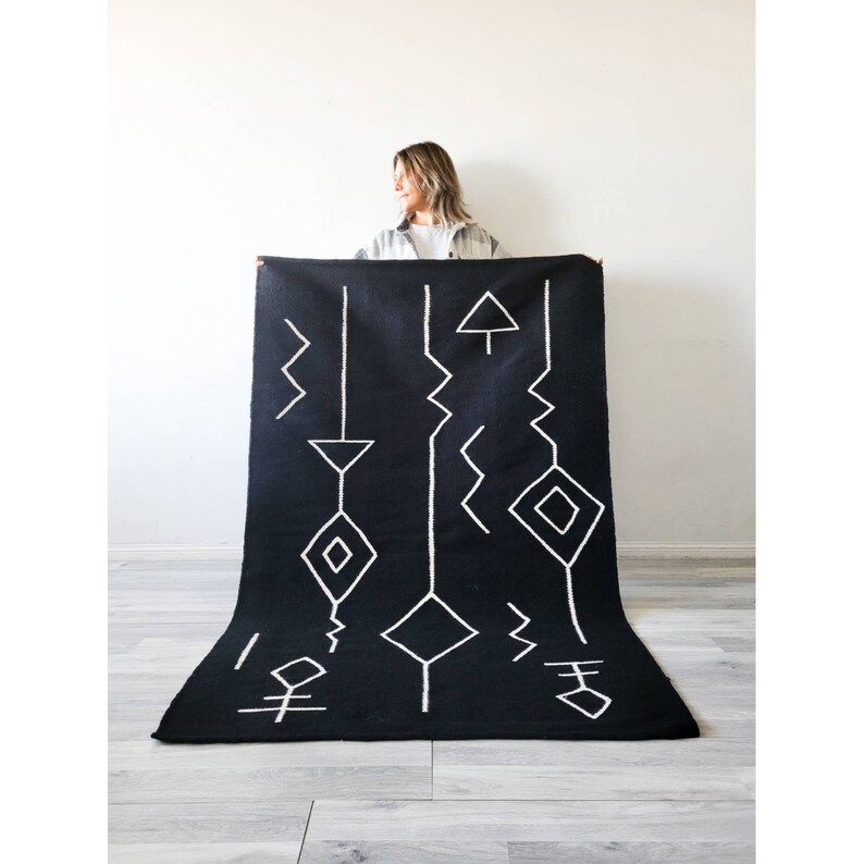 May include: Black and white geometric rug with a simple design. The rug is made of a soft, woven material and features a variety of geometric shapes, including diamonds, triangles, and zigzags.