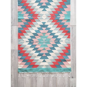 May include: A colorful geometric rug with a diamond pattern in shades of pink, blue, and red. The rug has a fringe border.