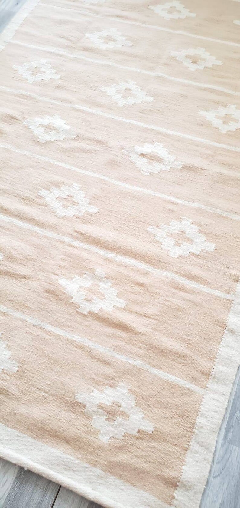 May include: A beige and white woven rug with a geometric pattern. The rug has a fringed border.