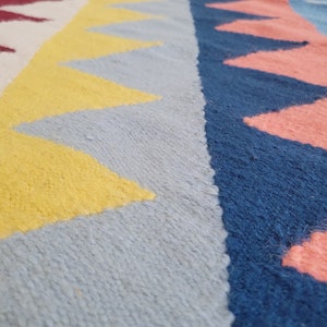 May include: Close-up of a colourful woven rug with geometric patterns in shades of yellow, blue, pink and red.