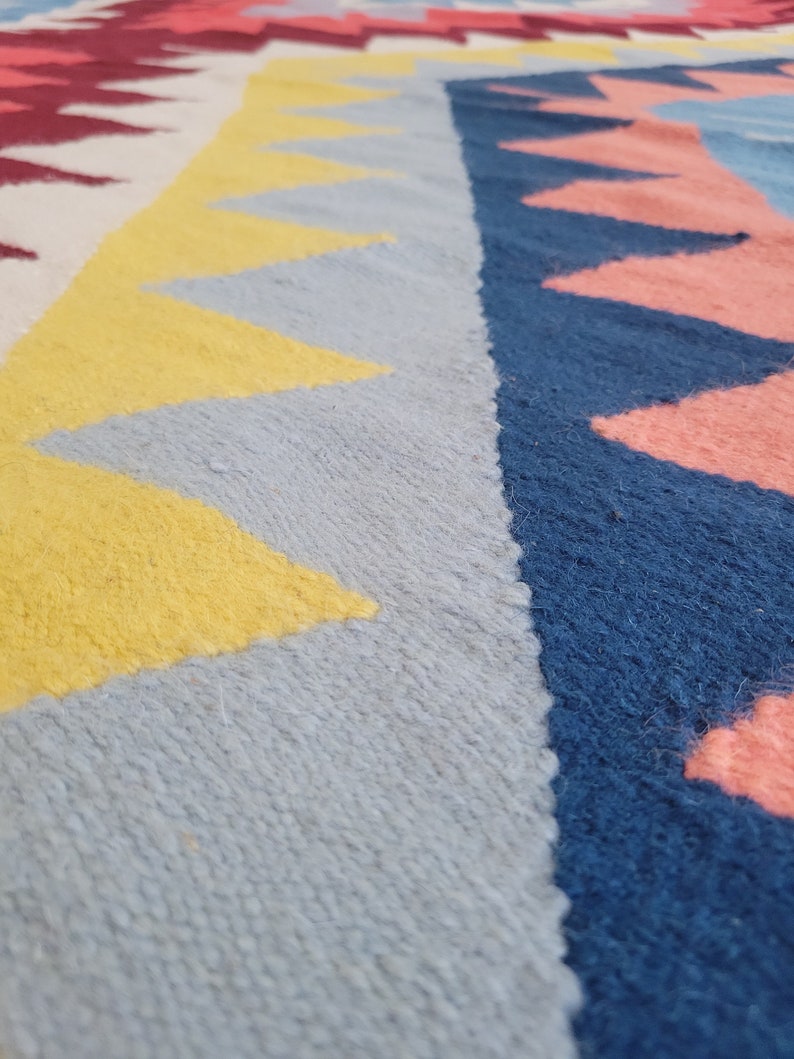 May include: Close-up of a colourful woven rug with geometric patterns in shades of yellow, blue, pink and red.