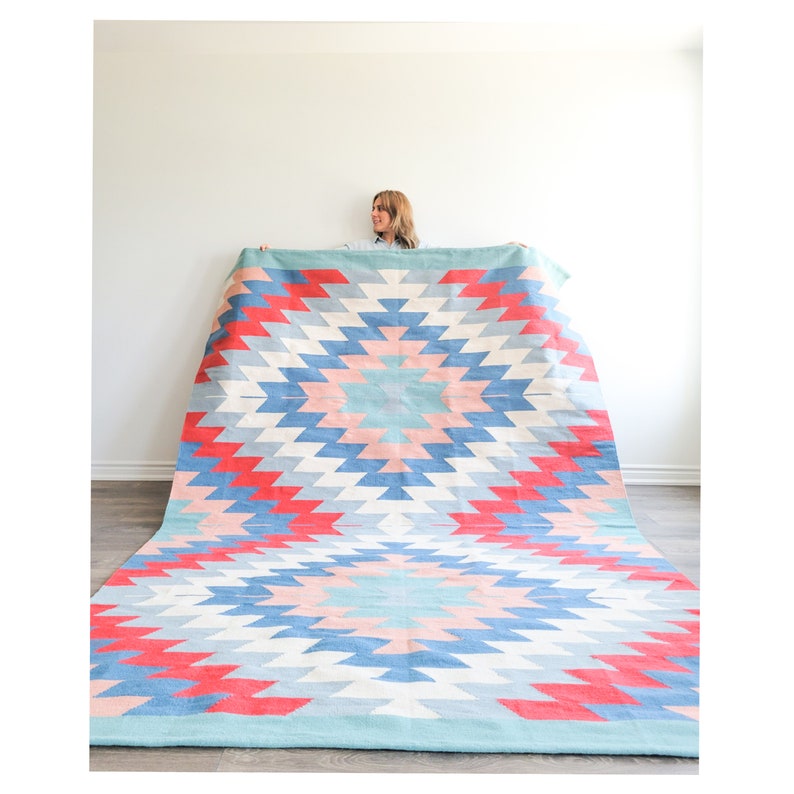 May include: A large, colorful rug with a geometric pattern in shades of blue, pink, and red. The rug has a starburst design in the center and is made of woven fabric.