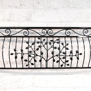 May include: Black wrought iron window or wall decor featuring a tree design. The rectangular frame has a decorative top with scrollwork. The tree design is in the center with vertical bars.