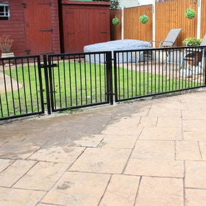 Puede incluir: Una valla de metal negro con dos puertas rodea un &aacute;rea de c&eacute;sped. La valla est&aacute; curvada en el extremo y tiene un patio de concreto en frente.