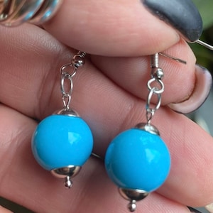 May include: A pair of silver dangle earrings with light blue round glass beads.