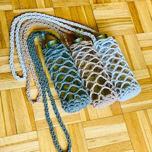 Può includere: Tre porta bottiglie all'uncinetto con cinturini. I porta bottiglie sono di colore grigio, beige e azzurro.