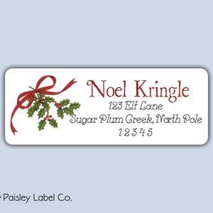 May include: A white rectangular label with a red ribbon and holly sprig design. The text on the label reads "Noel Kringle", "123 Elf Lane", "Sugar Plum Creek, North Pole", and "12345".