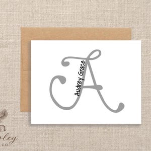 May include: A white card with a large gray letter "A" and the name "Audrey Grace" in a script font. The card is paired with a brown envelope, and the Paisley Label Co. logo is in the lower left corner.